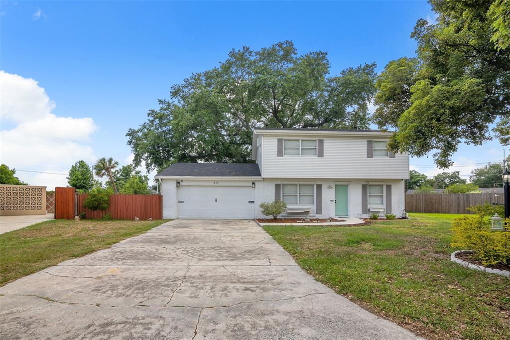 A two-story white house with a garage and a concrete driveway under a large tree — 215 KILMER LANE, WINTER HAVEN, FL