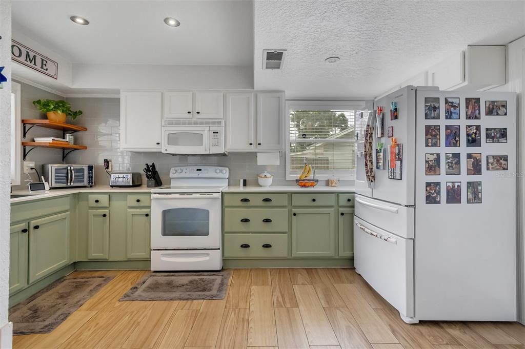 A kitchen features sage green lower cabinets, white upper cabinets, and light wood-look flooring — 215 KILMER LANE, WINTER HAVEN, FL