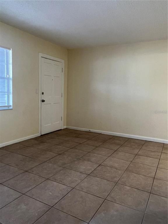 An empty room features beige walls, a white door, and brown square floor tiles — 2176 WINCHESTER ROAD N UNIT 2, ST PETERSBURG, FL