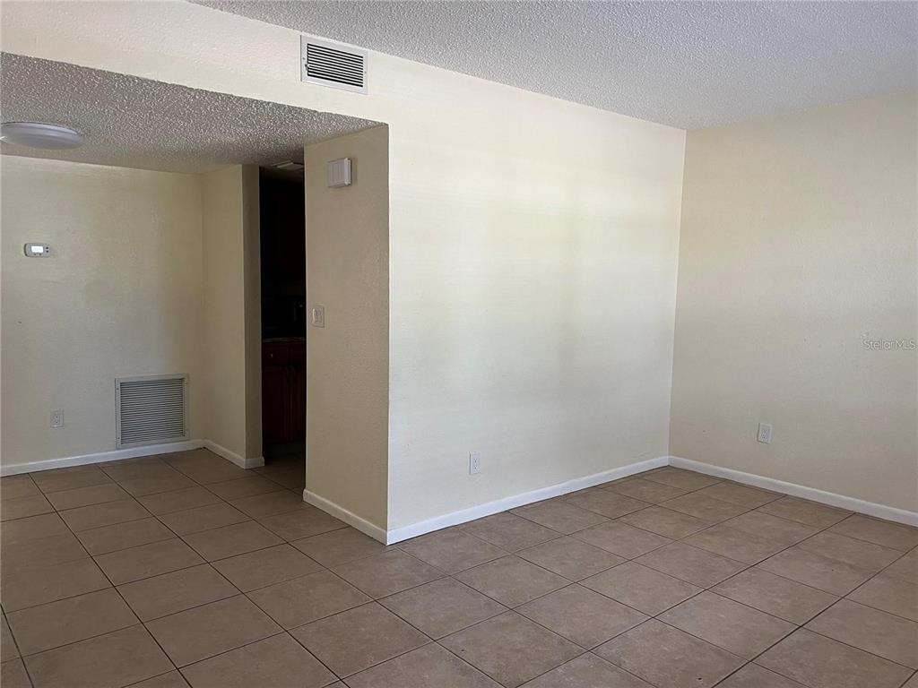 An empty room features beige tile flooring, light-colored walls, and a recessed kitchen entryway — 2176 WINCHESTER ROAD N UNIT 2, ST PETERSBURG, FL