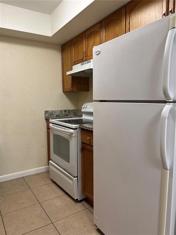 A kitchen features wood cabinets, a white stove, and a white refrigerator on tiled floors — 2176 WINCHESTER ROAD N UNIT 2, ST PETERSBURG, FL
