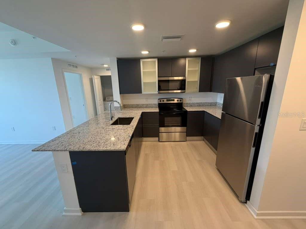A modern kitchen features dark cabinetry, granite countertops, and stainless steel appliances — 5587 MILLENIA PARK BOULEVARD UNIT 404, ORLANDO, FL