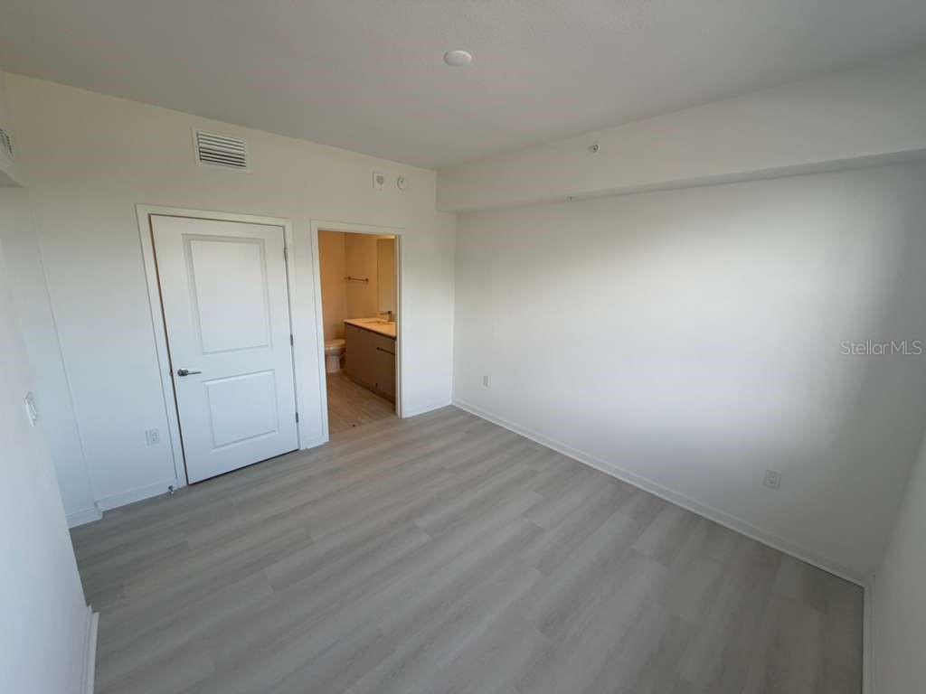 An empty bedroom features light-colored wood-look flooring, white walls, and an attached bathroom — 5587 MILLENIA PARK BOULEVARD UNIT 404, ORLANDO, FL