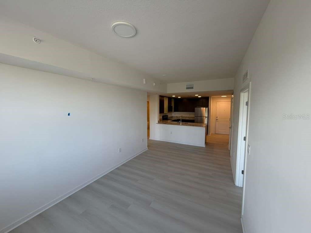 An open-concept living area features light wood-look flooring and a view into the kitchen — 5587 MILLENIA PARK BOULEVARD UNIT 404, ORLANDO, FL
