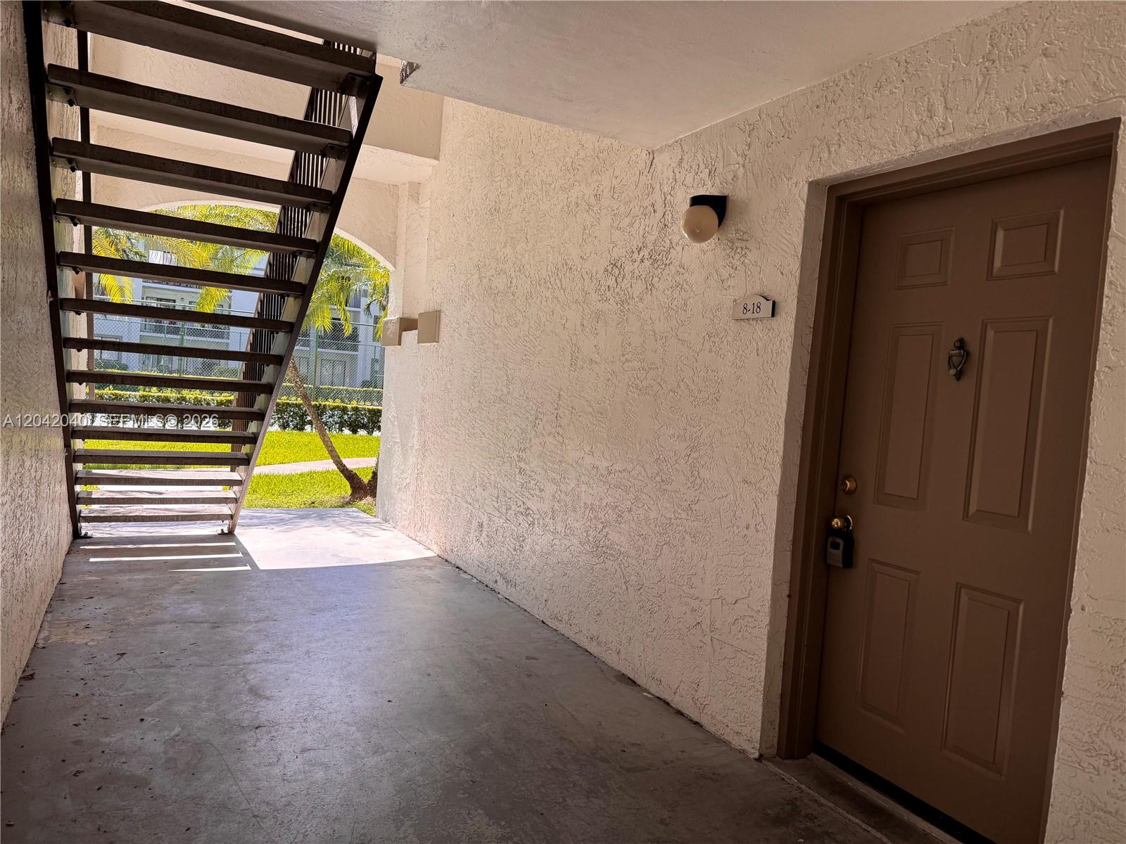 An outdoor apartment entryway features a brown door, a staircase, and textured white walls — 550 S Park Rd # 8, Hollywood FL 33021, HOLLYWOOD, FL