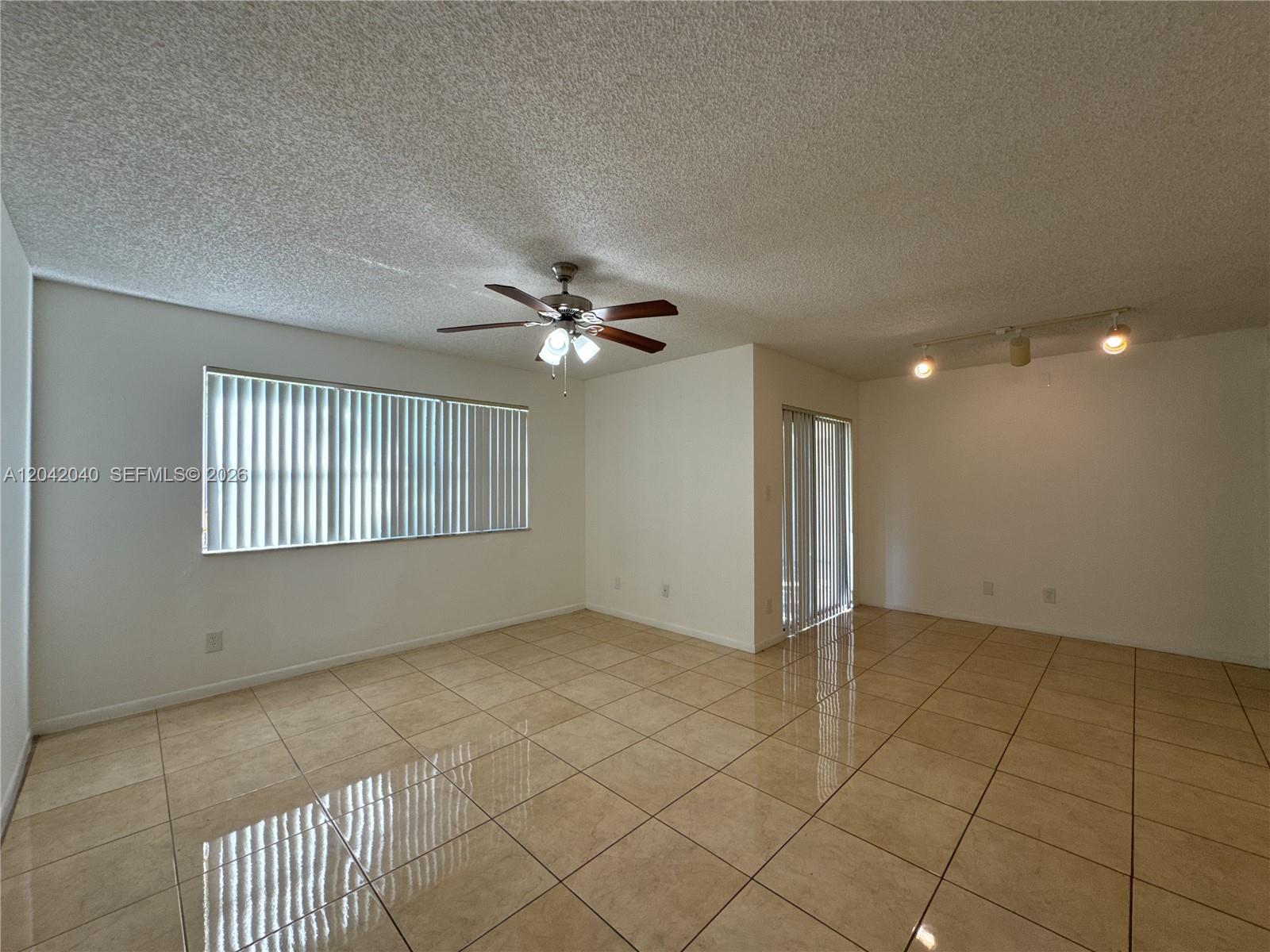 An empty living room features beige tile flooring, a ceiling fan, and vertical window blinds — 550 S Park Rd # 8, Hollywood FL 33021, HOLLYWOOD, FL