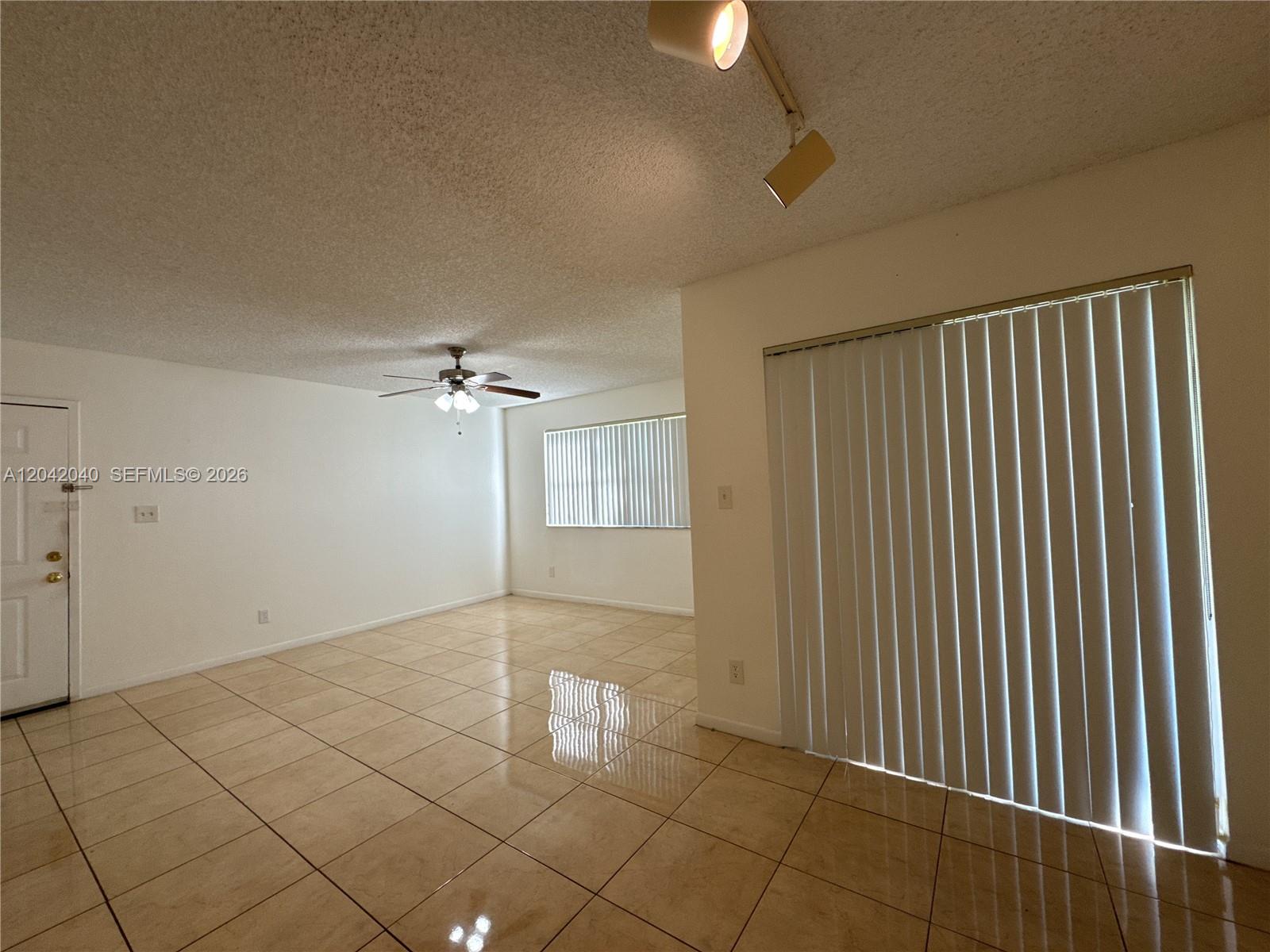 An empty living room features beige tile flooring, a ceiling fan, and vertical window blinds — 550 S Park Rd # 8, Hollywood FL 33021, HOLLYWOOD, FL
