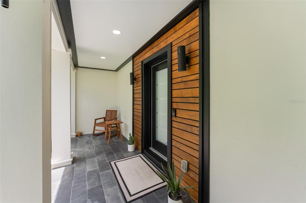 A covered entryway features a wood-paneled wall, a glass-paneled door, and dark stone flooring — 131 COUNTRYSIDE DRIVE, LONGWOOD, FL