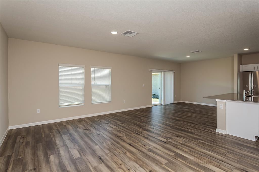 An open-concept living area features wood-look flooring, beige walls, and a sliding glass door — 5449 SAN PIETRO DRIVE, WINTER HAVEN, FL