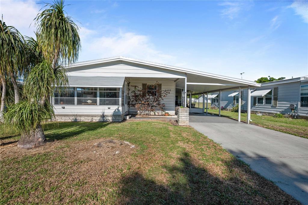A single-story manufactured home with a carport and a palm tree in the front yard — 5427 SEVILLE DRIVE, ZEPHYRHILLS, FL