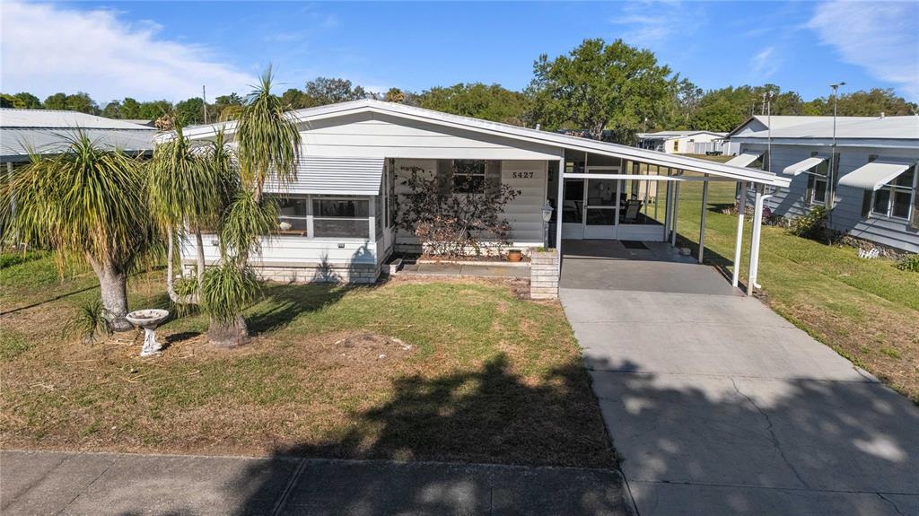 A single-story mobile home with a white exterior, a carport, and a front lawn — 5427 SEVILLE DRIVE, ZEPHYRHILLS, FL