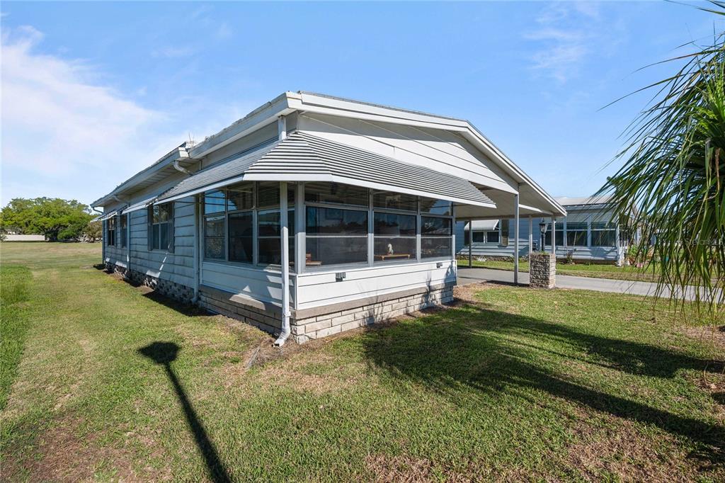 An exterior view of a single-story mobile home with a screened-in porch and attached carport — 5427 SEVILLE DRIVE, ZEPHYRHILLS, FL