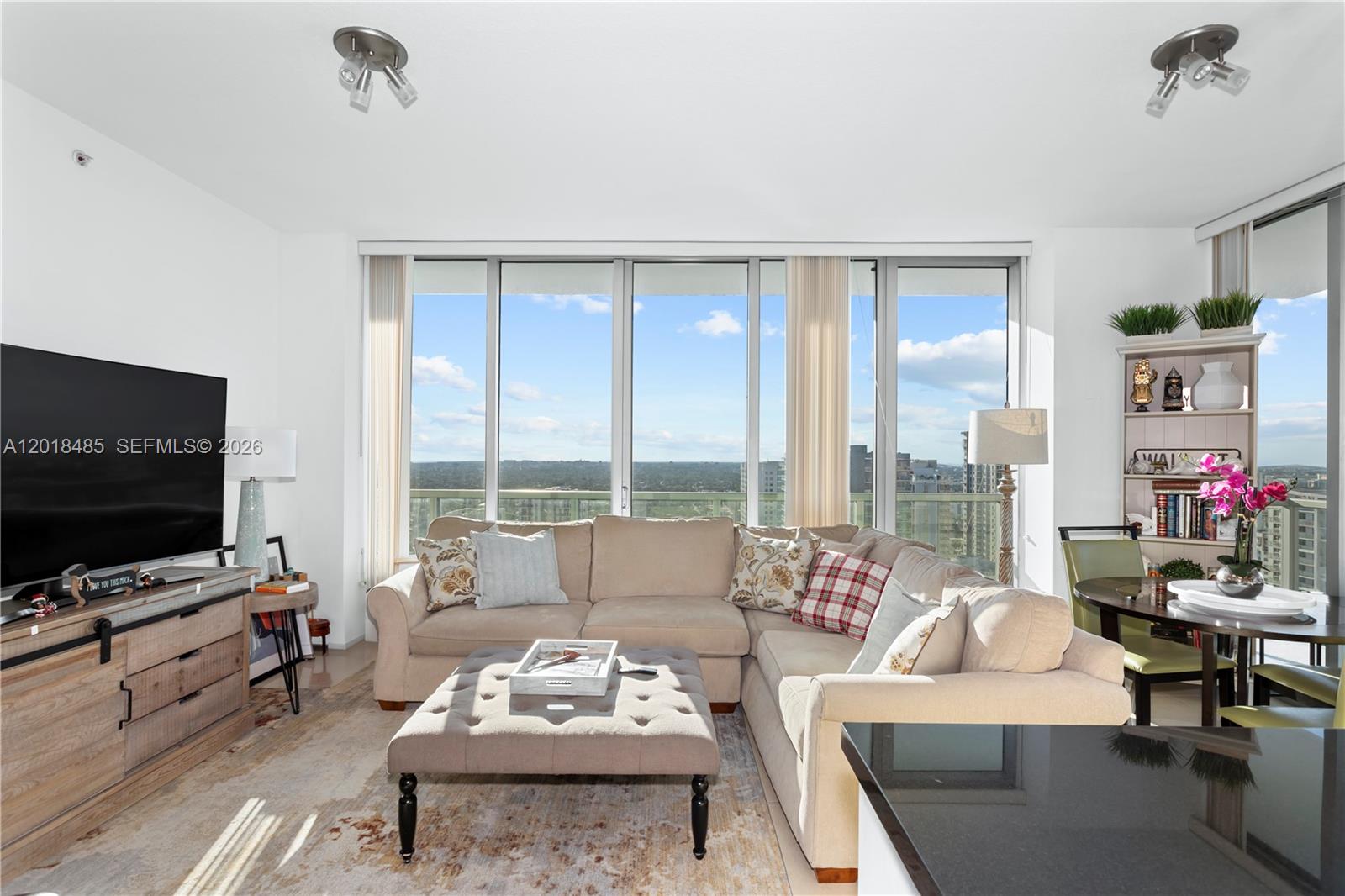 A living room features a beige sectional sofa, a tufted ottoman, and floor-to-ceiling windows — 1111 SW 1st Ave, Miami FL 33130, MIAMI, FL