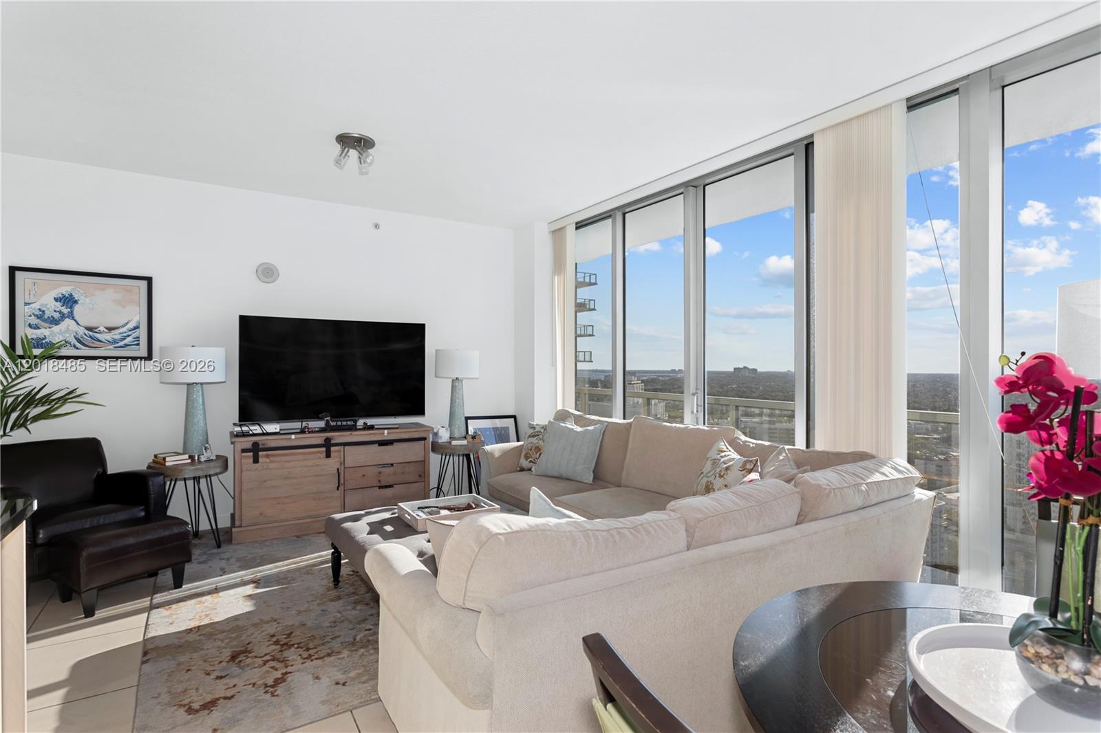 A living room features a beige sectional sofa, a television console, and floor-to-ceiling windows — 1111 SW 1st Ave, Miami FL 33130, MIAMI, FL