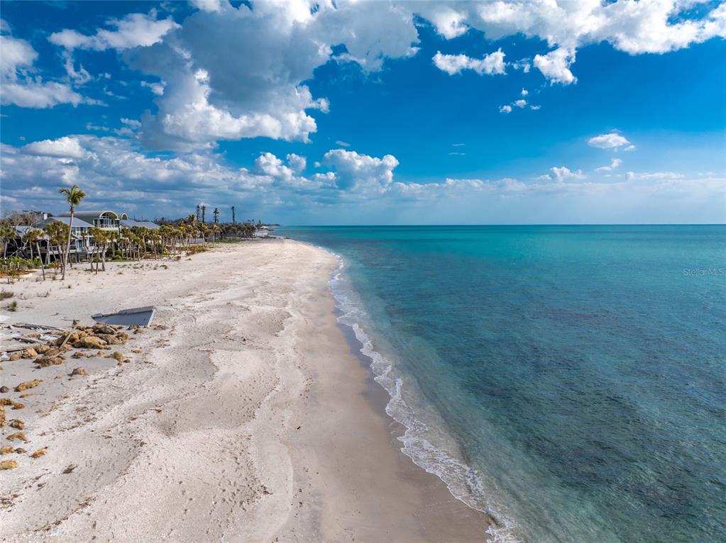 An aerial view shows a sandy beach along a turquoise ocean with coastal houses nearby — 7380 MANASOTA KEY ROAD, ENGLEWOOD, FL