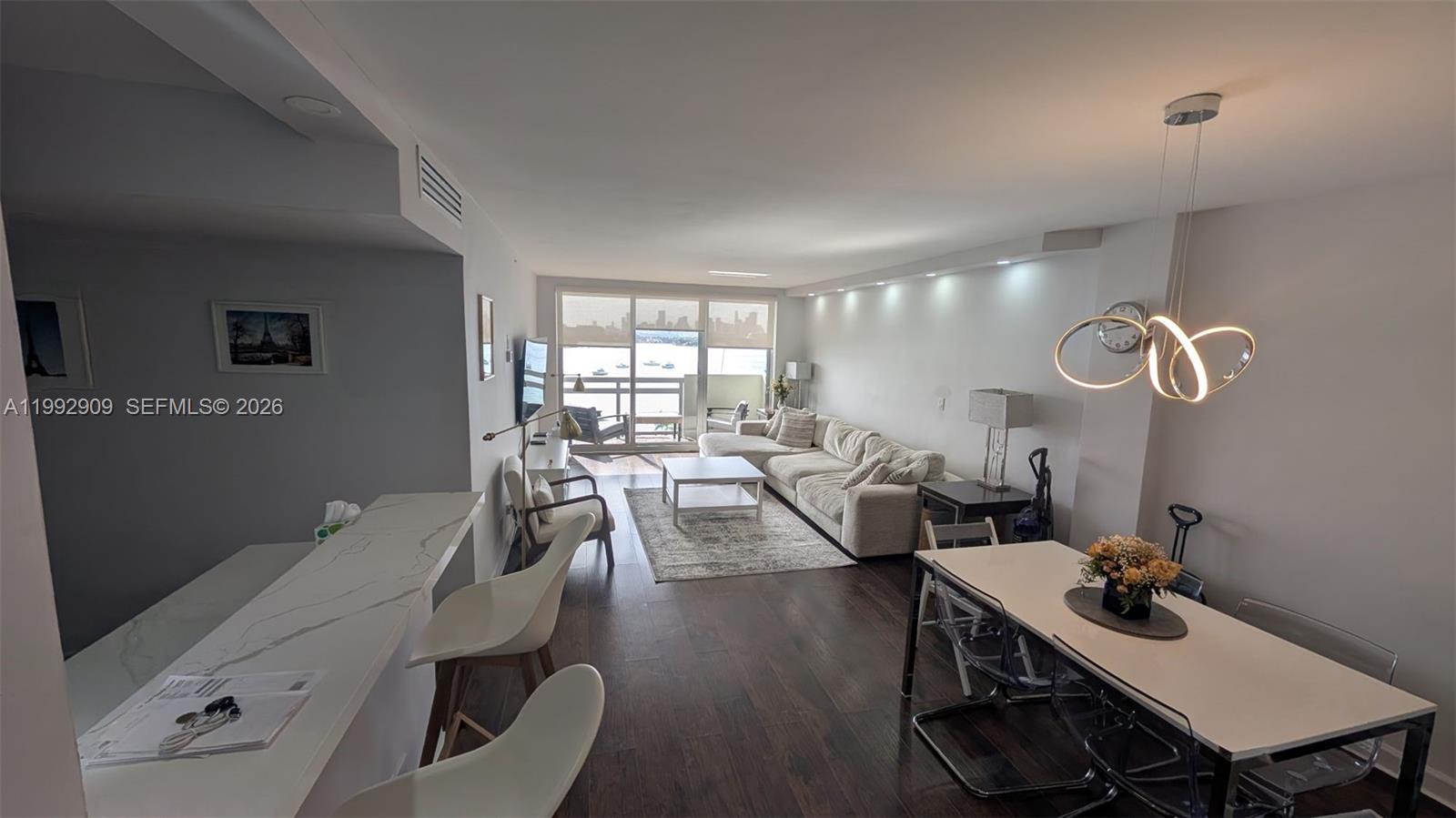 An open-concept living and dining area features dark wood floors, modern lighting, and balcony views — 1500 Bay Rd # 822S, Miami Beach FL 33139, MIAMI BEACH, FL