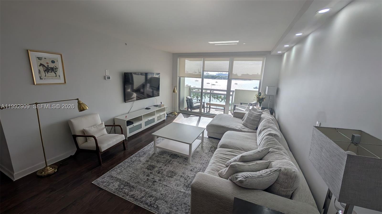 A modern living room features a sectional sofa, white coffee table, and balcony water views — 1500 Bay Rd # 822S, Miami Beach FL 33139, MIAMI BEACH, FL
