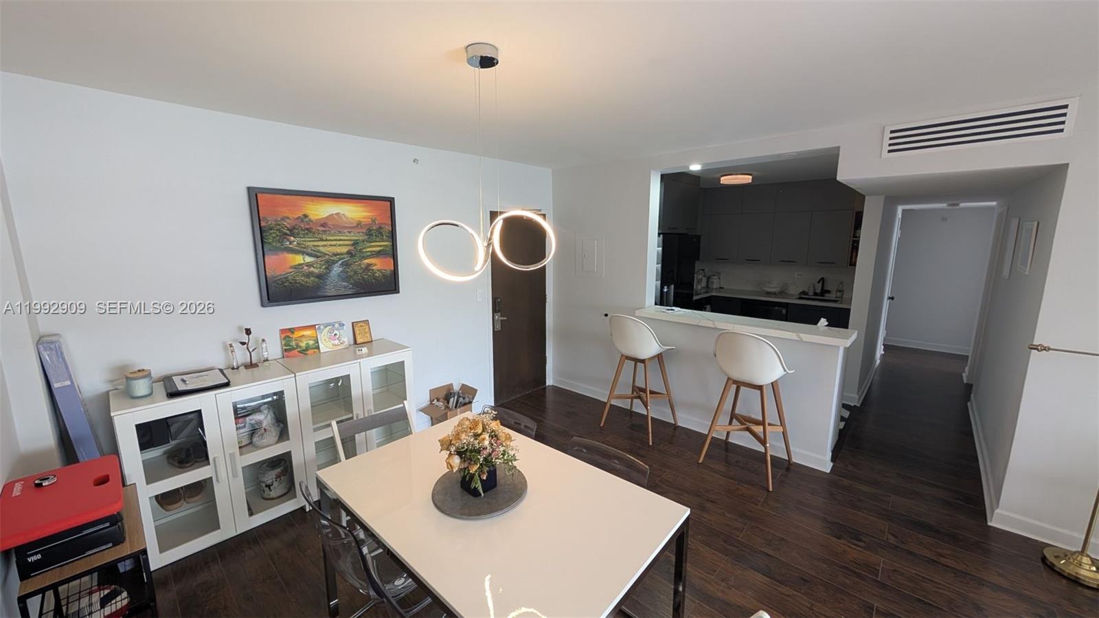 A dining area with a white table and modern light fixture opens to a kitchen — 1500 Bay Rd # 822S, Miami Beach FL 33139, MIAMI BEACH, FL