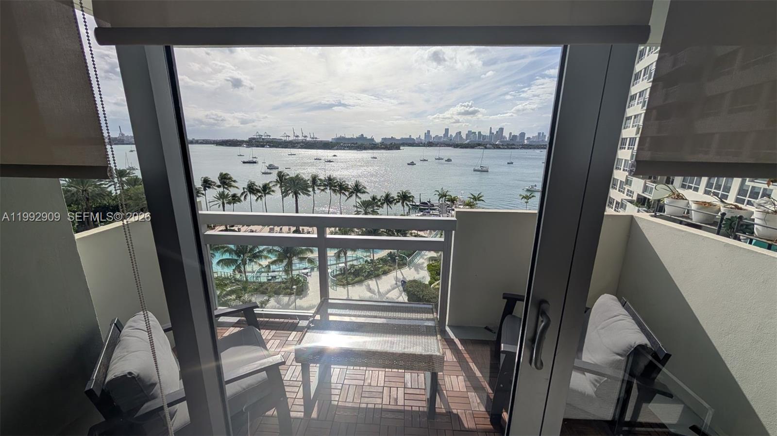 A balcony with outdoor furniture overlooks a swimming pool, a bay, and a city skyline — 1500 Bay Rd # 822S, Miami Beach FL 33139, MIAMI BEACH, FL