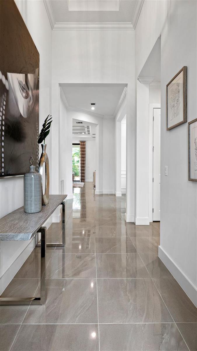 A bright hallway features large gray tile flooring, a console table, and framed wall art — 1911 SE Royale Preserve Way, Stuart FL 34997, STUART, FL