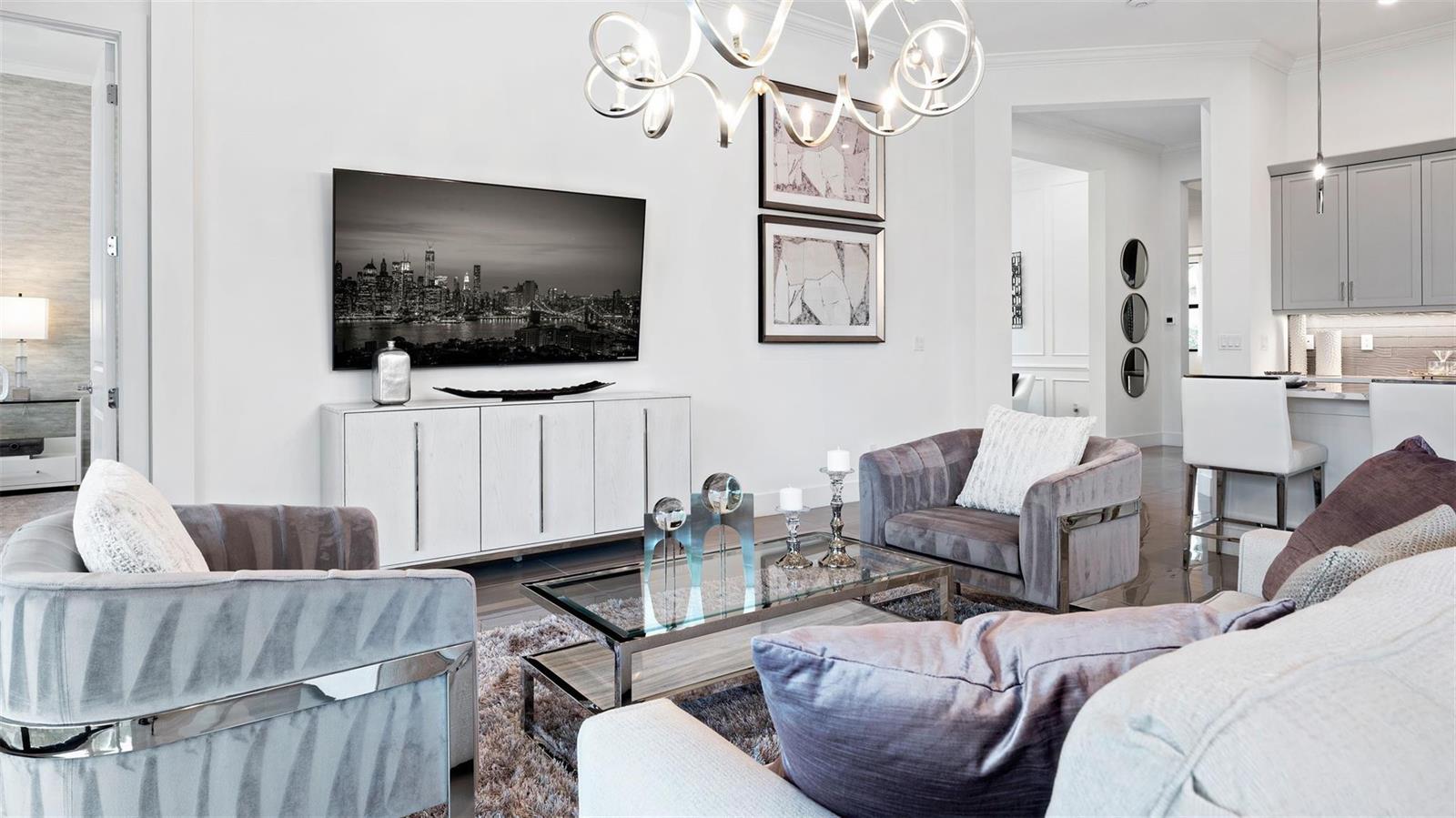 A modern living room features gray velvet armchairs, a glass coffee table, and a wall-mounted television — 1911 SE Royale Preserve Way, Stuart FL 34997, STUART, FL