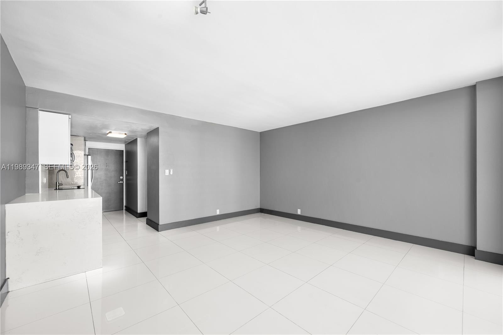 A bright, empty room features gray walls, white tile flooring, and an open kitchen area — 3301 NE 5th AVE # 1212, Miami FL 33137, MIAMI, FL