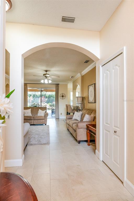 A tiled hallway leads through an arched entryway into a living room with beige furniture — 10755 NORTHRIDGE COURT, TRINITY, FL