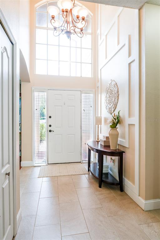 A bright entryway features a white front door, a chandelier, and a dark wood console table — 10755 NORTHRIDGE COURT, TRINITY, FL