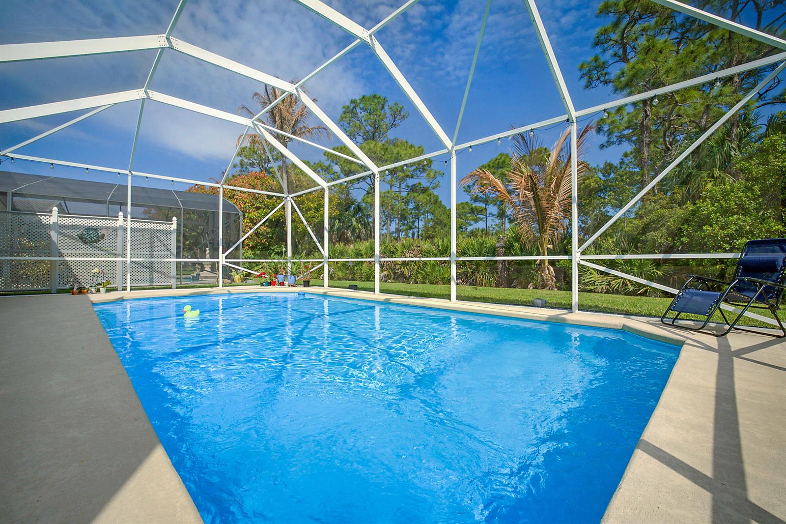 A swimming pool with a screen enclosure sits in a backyard with trees and landscaping — 7004 SE Twin Oaks Circle, Stuart FL 34997, STUART, FL