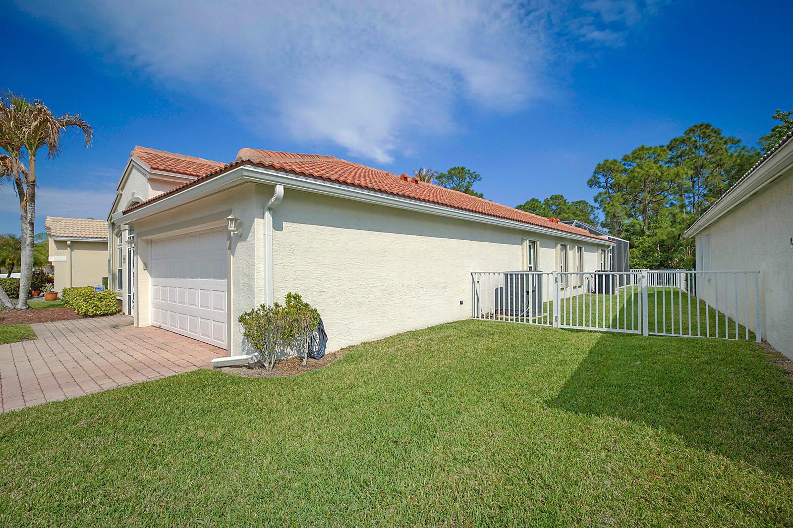 The exterior of a beige house with a red tile roof and a white fence — 7004 SE Twin Oaks Circle, Stuart FL 34997, STUART, FL