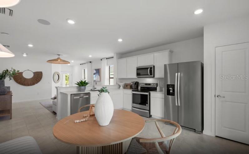 A kitchen with white cabinets and stainless steel appliances opens into a dining area — 810 BALLEBY TRAIL, BRADENTON, FL