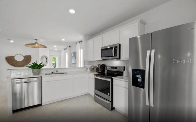 A modern kitchen features white cabinetry, stainless steel appliances, and a light-colored tile floor — 810 BALLEBY TRAIL, BRADENTON, FL