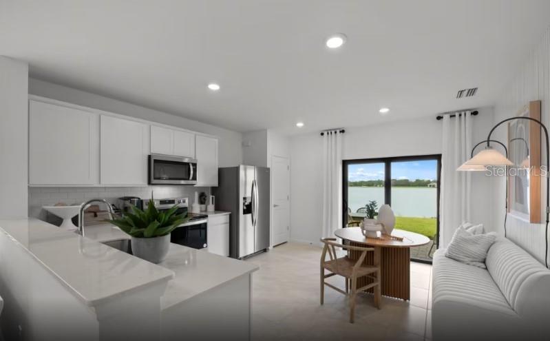 A kitchen with white cabinets and stainless steel appliances opens to a dining area outdoors — 810 BALLEBY TRAIL, BRADENTON, FL