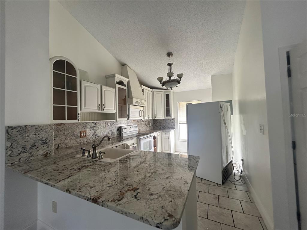 A kitchen features white cabinets, granite countertops, a sink, and a white refrigerator — 3651 N GOLDENROD ROAD UNIT 206, WINTER PARK, FL