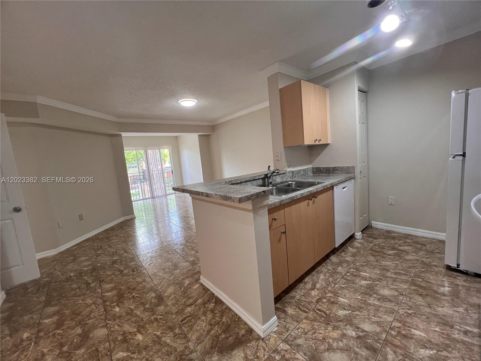 A kitchen with light wood cabinets and a breakfast bar overlooks an open living area — 2496 Centergate Dr # 205, Miramar FL 33025, MIRAMAR, FL