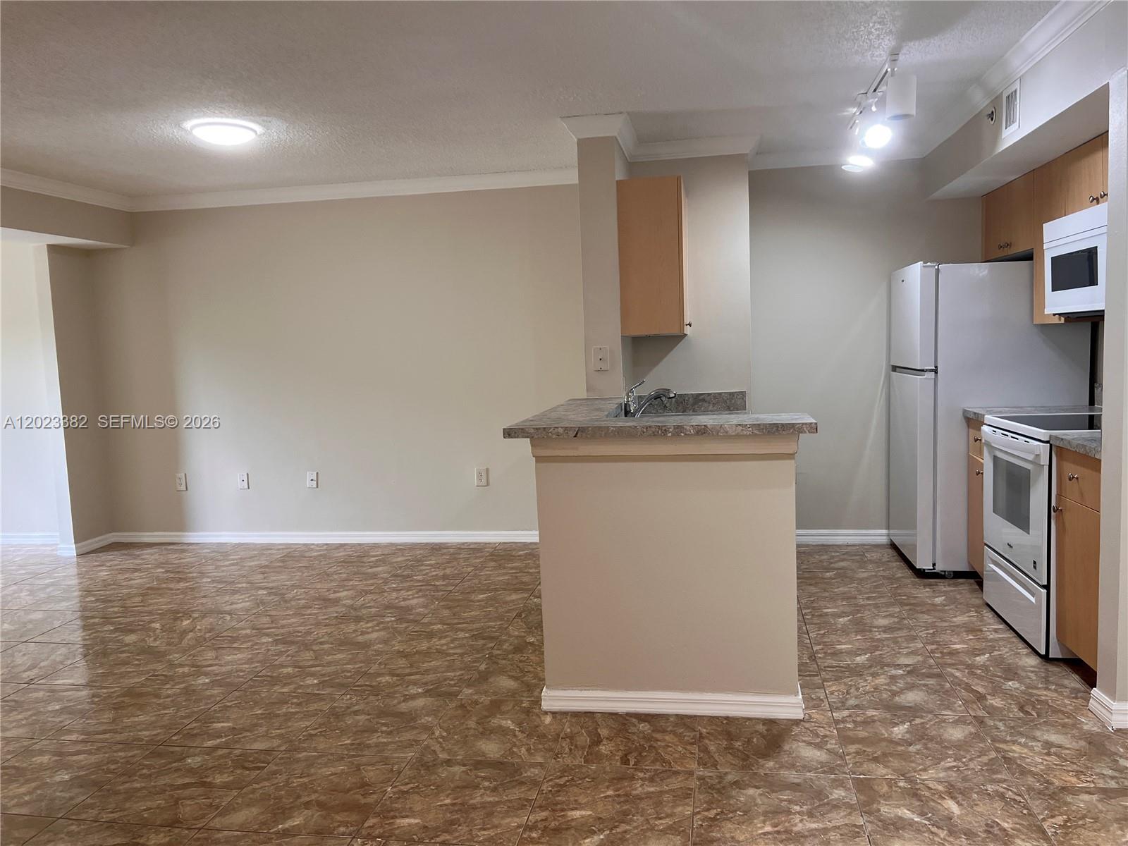 A kitchen with light wood cabinets, white appliances, and a tiled floor opens to a room — 2496 Centergate Dr # 205, Miramar FL 33025, MIRAMAR, FL