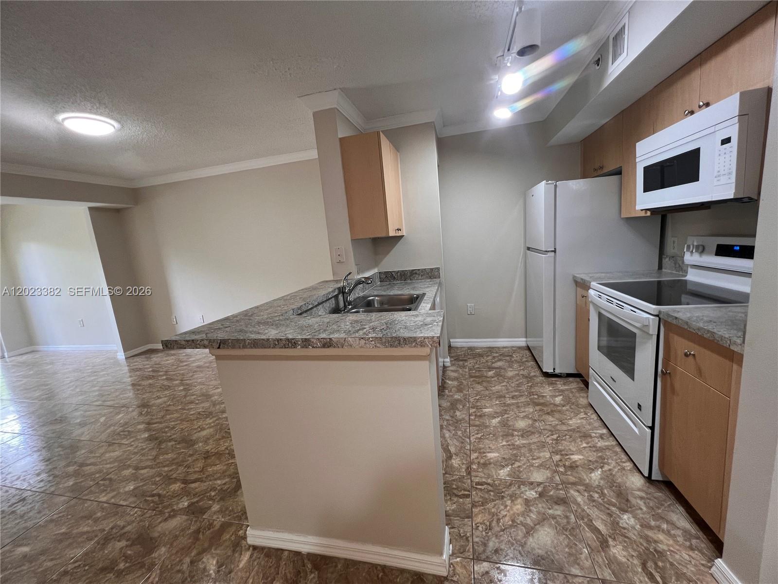 A kitchen features light wood cabinets, a granite-look countertop, and white appliances on tiled floors — 2496 Centergate Dr # 205, Miramar FL 33025, MIRAMAR, FL