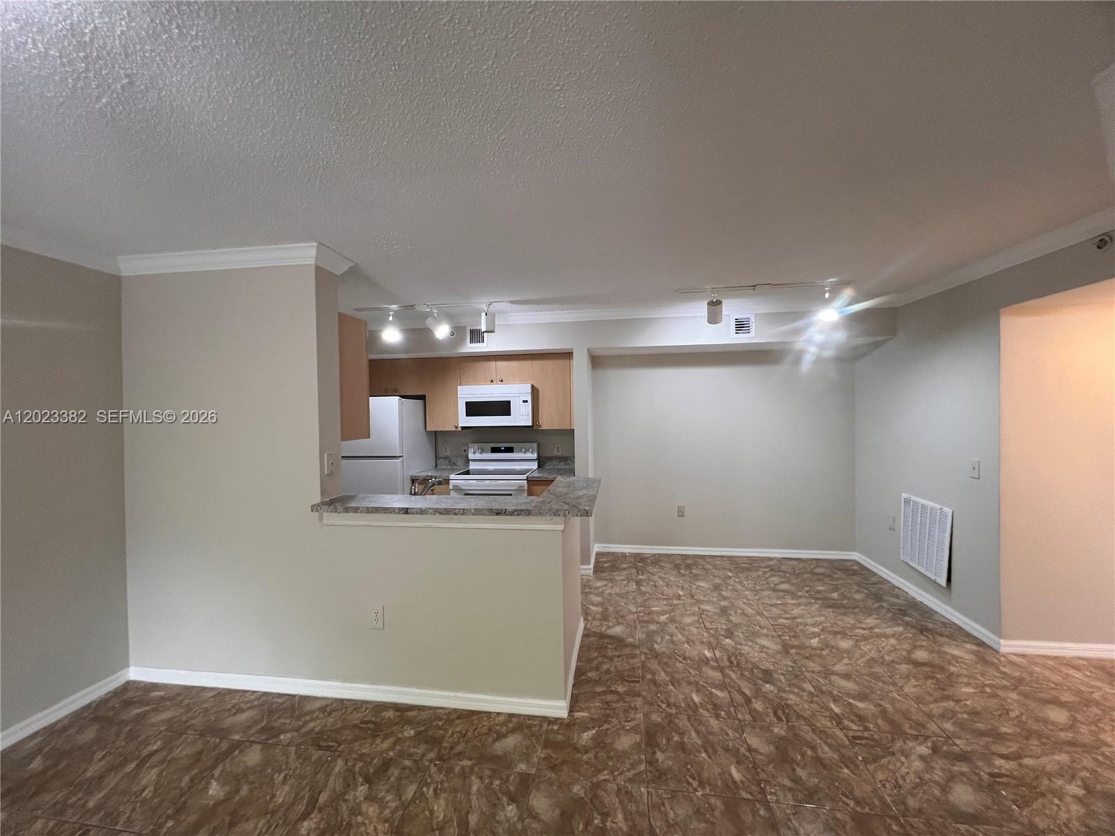 An open-concept kitchen with light wood cabinets and a breakfast bar overlooks a tiled room — 2496 Centergate Dr # 205, Miramar FL 33025, MIRAMAR, FL