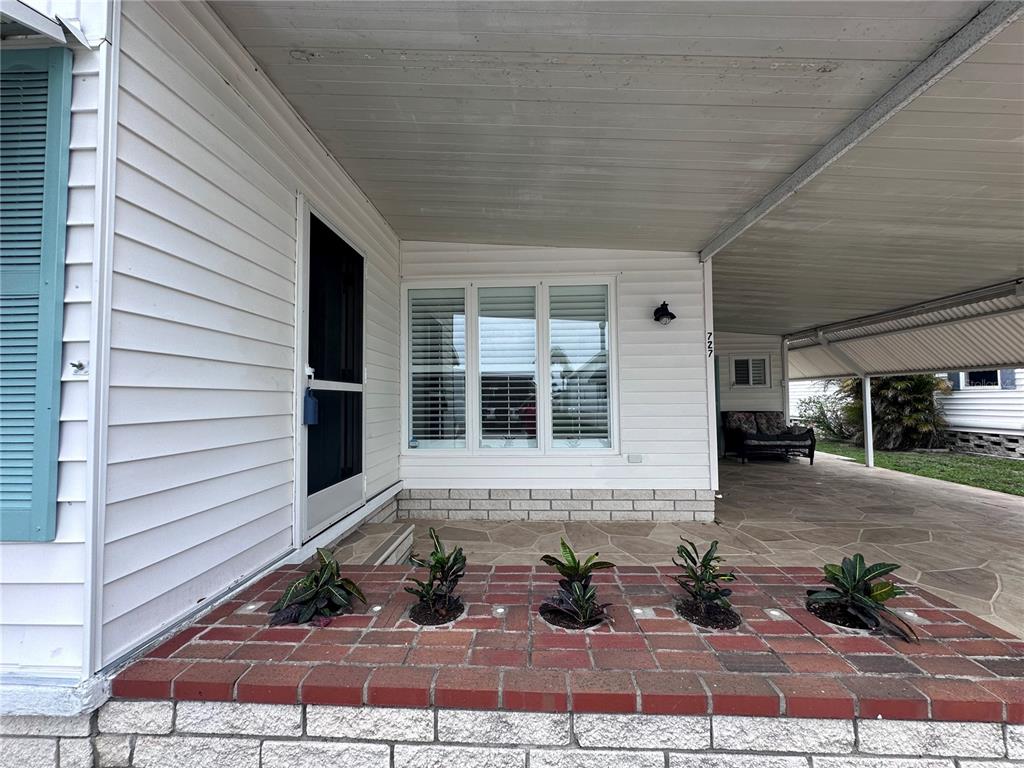 A white house exterior features a brick planter box with small plants and a carport — 1100 BELCHER ROAD S UNIT 727, LARGO, FL