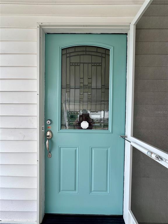 A teal front door with a decorative glass window is set against white siding — 1100 BELCHER ROAD S UNIT 727, LARGO, FL