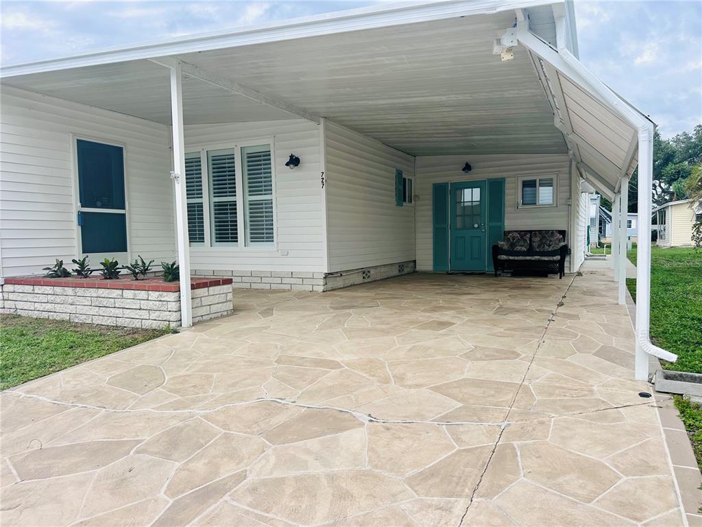 A white mobile home features a stone-patterned concrete carport and a teal front door — 1100 BELCHER ROAD S UNIT 727, LARGO, FL