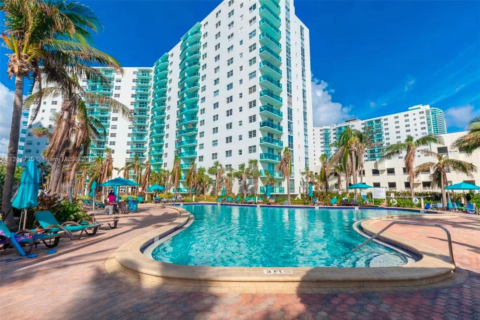 A swimming pool with lounge chairs sits in front of a tall white apartment building — 3901 S Ocean Dr # 11C, Hollywood FL 33019, HOLLYWOOD, FL