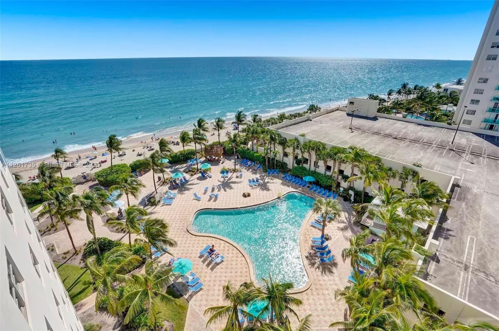 An aerial view of a resort swimming pool, palm trees, and a beach along the ocean — 3901 S Ocean Dr # 11C, Hollywood FL 33019, HOLLYWOOD, FL