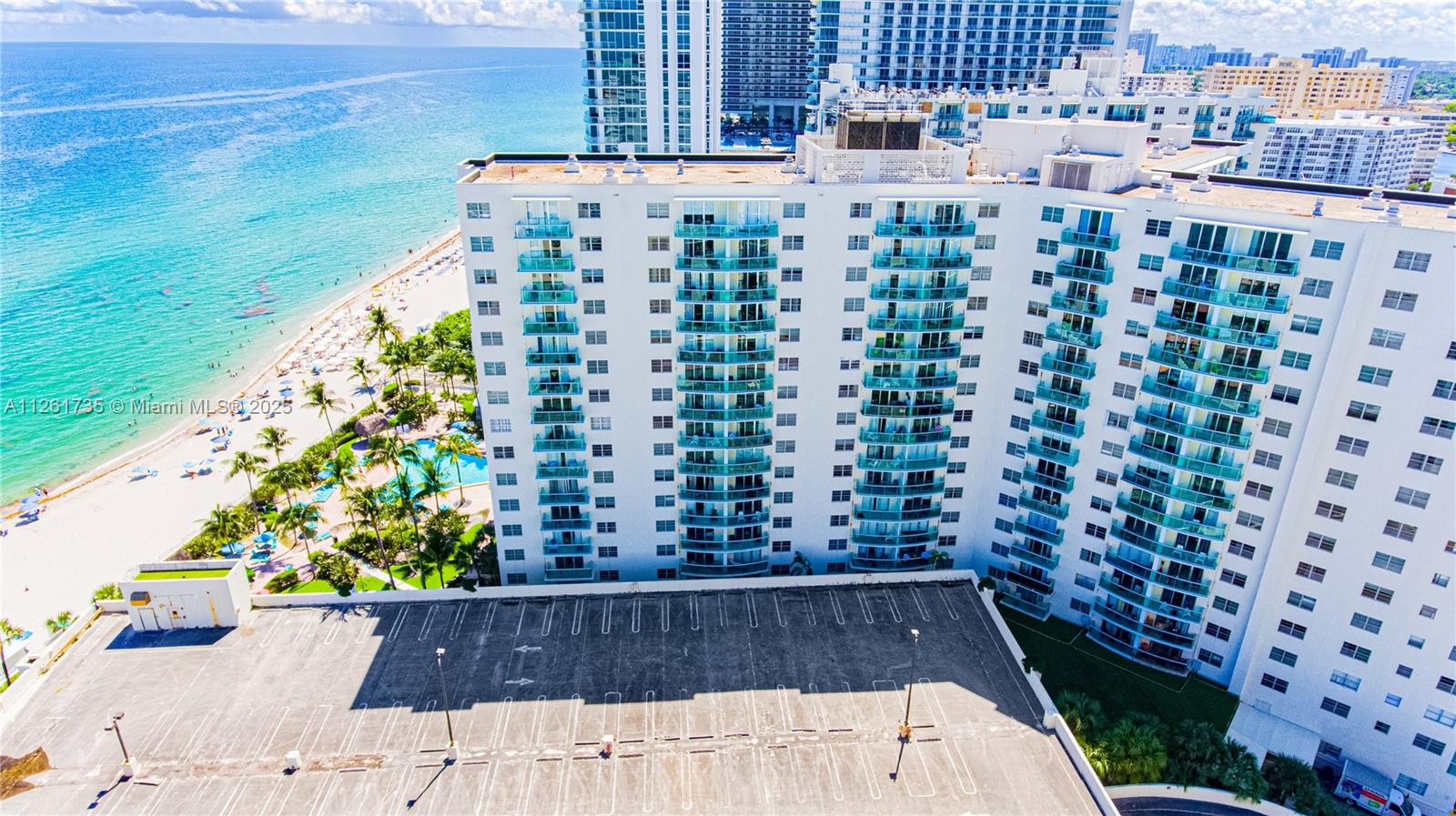 An aerial view shows a high-rise residential building next to a beach and parking lot — 3901 S Ocean Dr # 11C, Hollywood FL 33019, HOLLYWOOD, FL