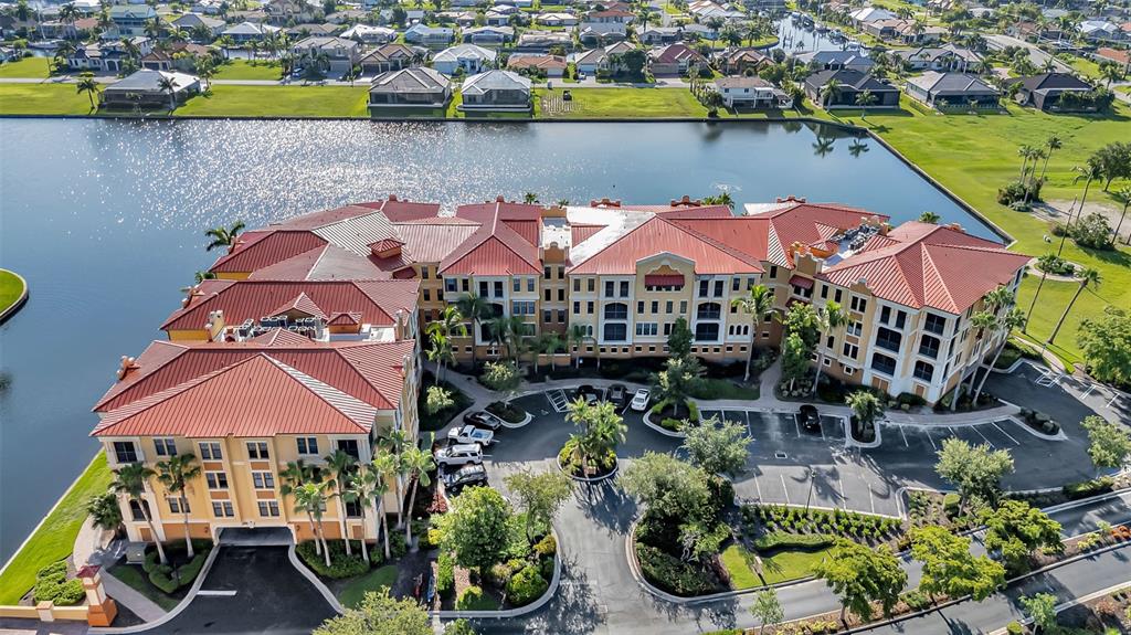 An aerial view shows a multi-story apartment building with a red roof beside a lake — 98 VIVANTE BOULEVARD UNIT 98412, PUNTA GORDA, FL