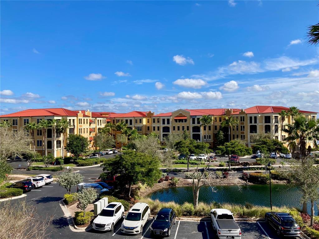 An exterior view of a multi-story apartment complex with red roofs, a parking lot, and a pond — 98 VIVANTE BOULEVARD UNIT 98412, PUNTA GORDA, FL