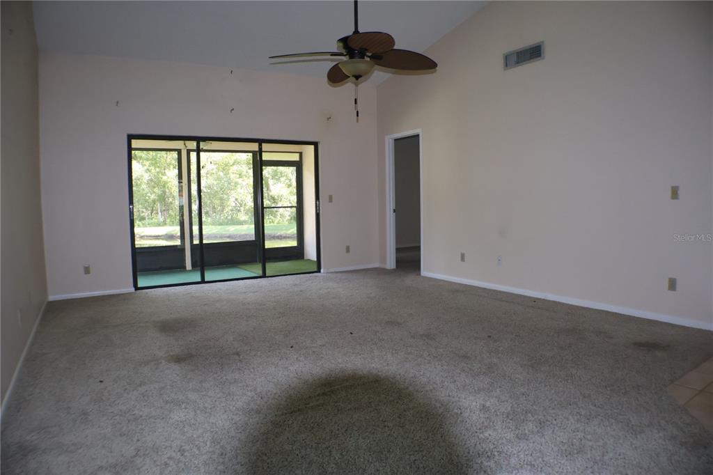 An empty living room features beige carpet, a ceiling fan, and sliding doors to a lanai — 11806 WHITE ASH DRIVE, NEW PORT RICHEY, FL