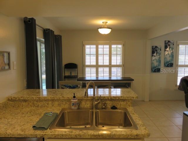 A kitchen sink with granite countertops overlooks a dining area with plantation shutters and curtains — 7207 15TH AVENUE DRIVE W, BRADENTON, FL