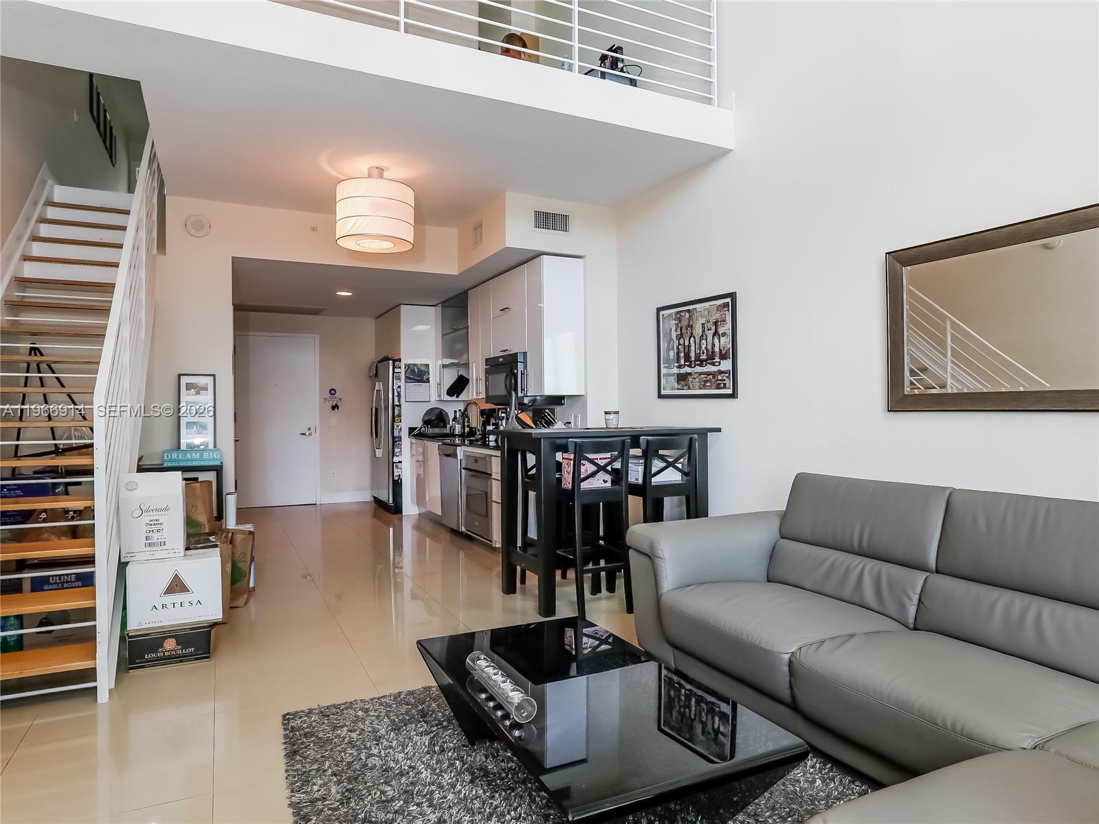 A modern living room and kitchen area features a staircase, high ceilings, and tile flooring — 60 SW 13th St # 3404, Miami FL 33130, MIAMI, FL