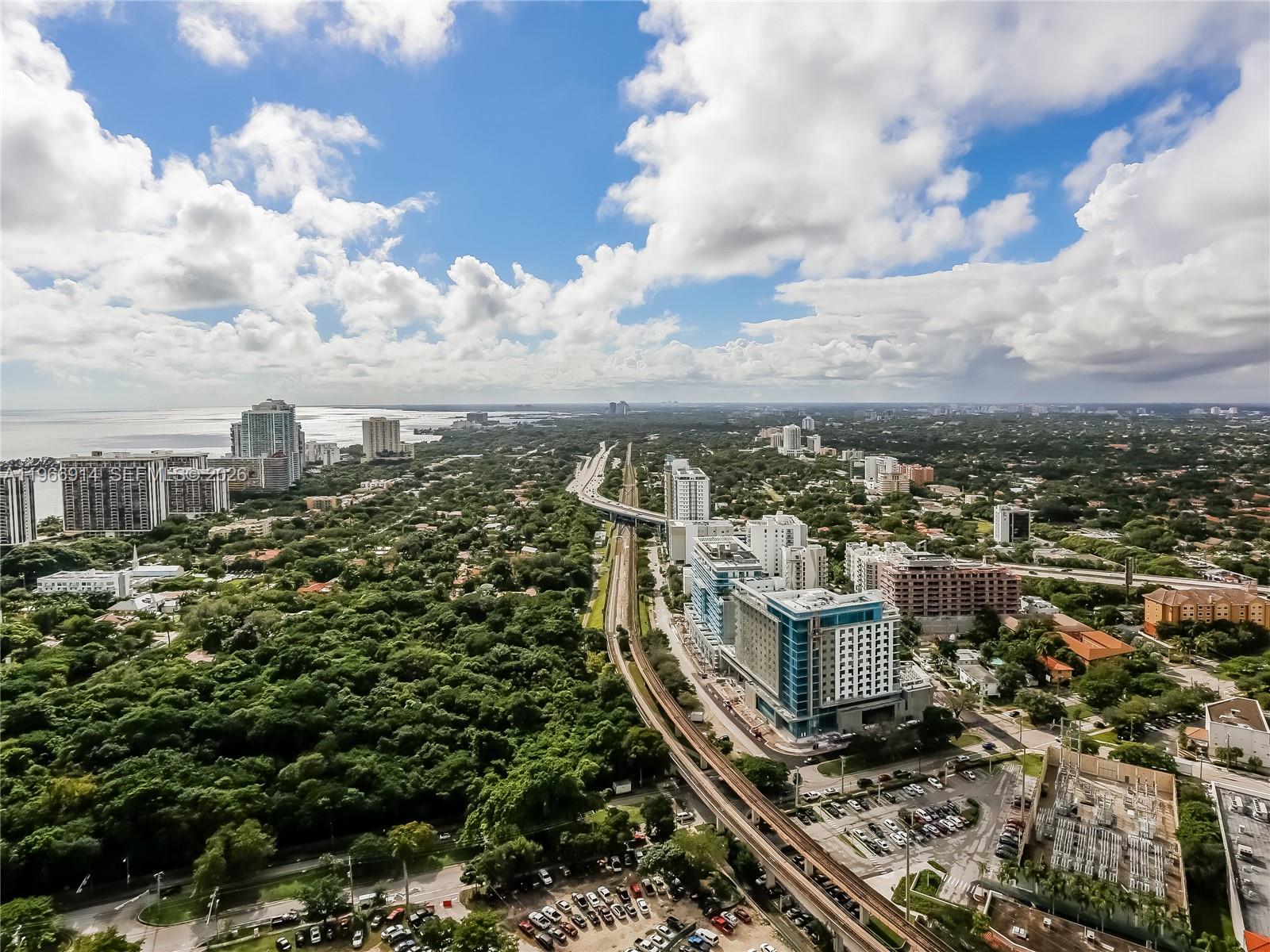 An aerial view shows a city skyline, a railway line, and dense trees near water — 60 SW 13th St # 3404, Miami FL 33130, MIAMI, FL